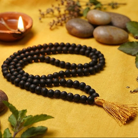 Black beaded necklace with tassel on a yellow surface with stones and plants
