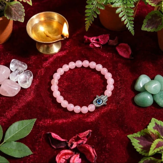 Pink beaded bracelet with a silver charm on a red fabric background with plants and stones.
