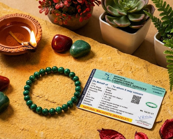 Green beaded bracelet, small bowl with a candle, stones, and a card on a stone surface with plants.