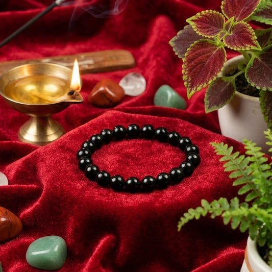 Black beaded bracelet on a red cloth with incense, crystals, and plants.