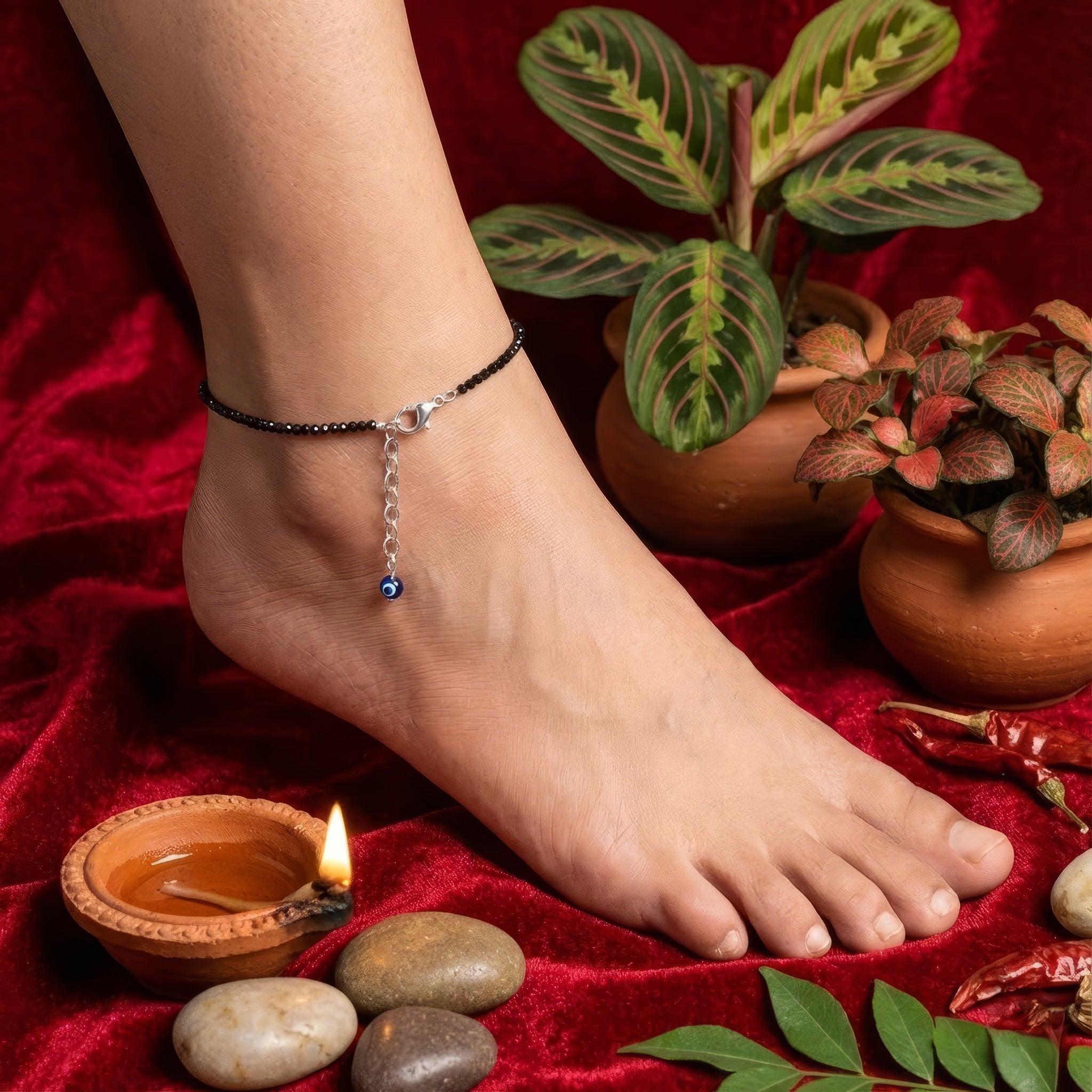 Anchored foot with a anklet on a red fabric background with plants and stones.