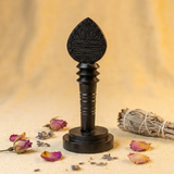 Black decorative object with a lotus design on a beige background with dried flowers and sage.