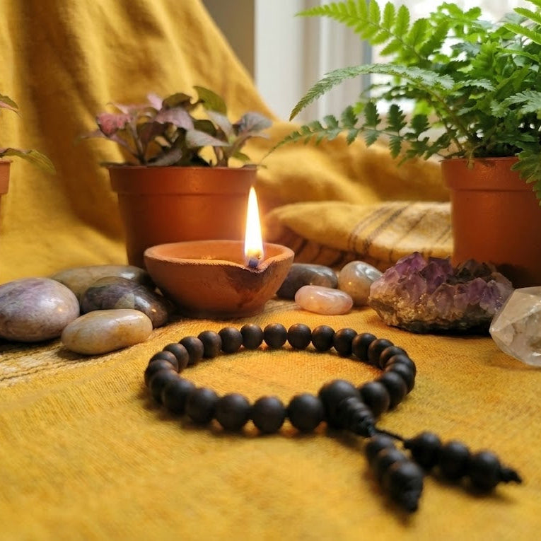 Black beaded bracelet on a yellow surface with potted plants and a lit candle in the background.