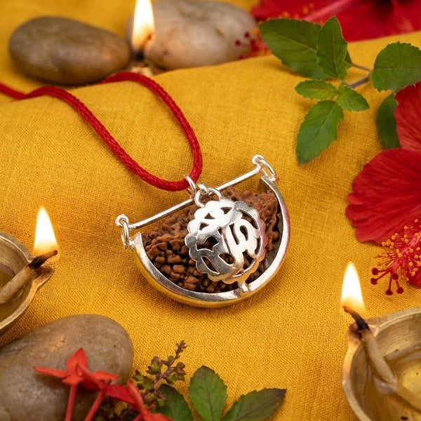 Silver necklace with a pendant on a yellow fabric background with candles and flowers.