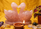 Pink crystal swans with stones and a candle on a yellow fabric background