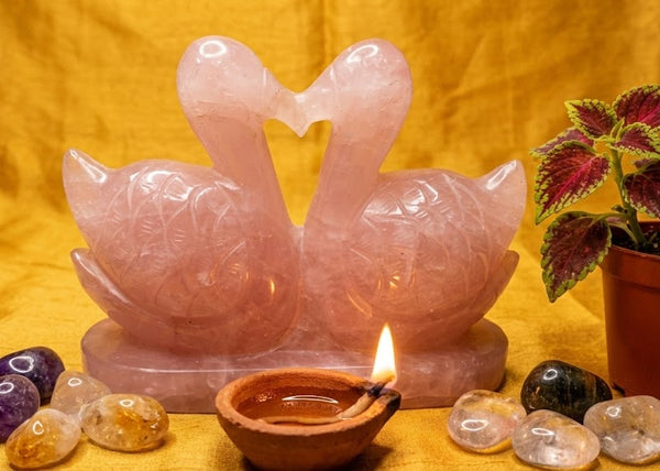 Pink crystal swans with stones and a candle on a yellow fabric background