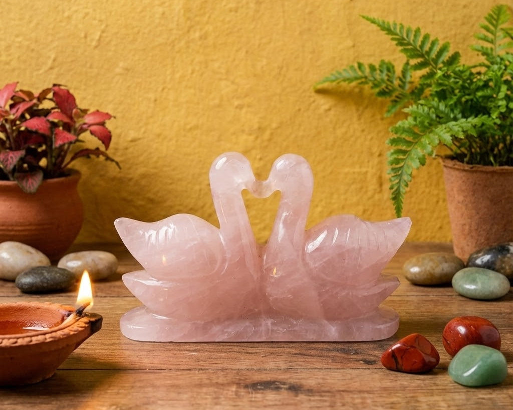 Rose quartz swan sculpture on a wooden surface with plants and stones.