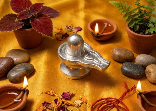 Silver Shiva lingam with candles, stones, and plants on a yellow fabric background