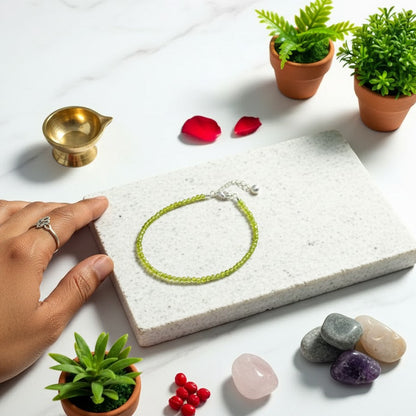 Hand holding a green bracelet on a stone surface with small plants and stones around