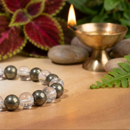 Beaded necklace on a wooden surface with a candle and plants in the background