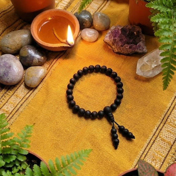 Black beaded bracelet on a yellow cloth with plants and stones around