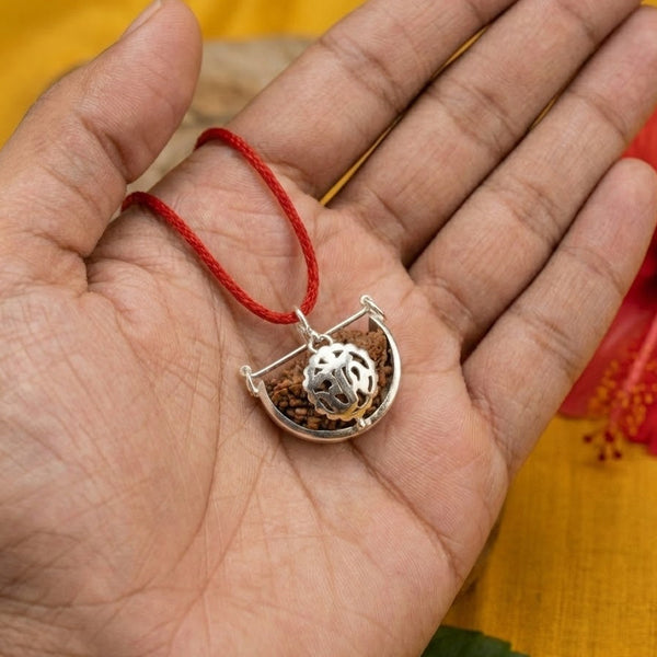 Hand holding a silver pendant with red string on a yellow background with a red flower.