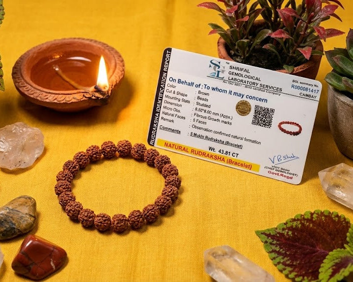Bracelet, crystals, and a lit oil lamp on a yellow surface with a card in the background.