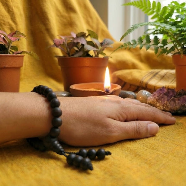 Hand with a beaded bracelet on a yellow surface with plants and crystals