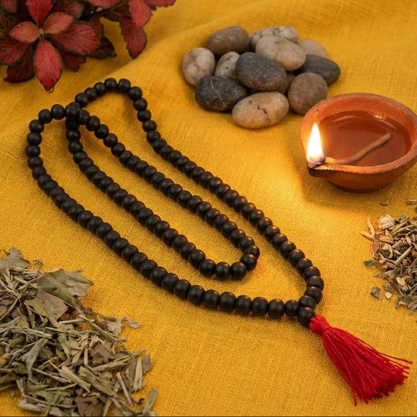 Black beaded necklace with a red tassel on a yellow fabric background with stones, leaves, and a lit candle.