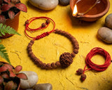 Bracelets with red strings, a small lamp, and stones on a yellow surface with plants.