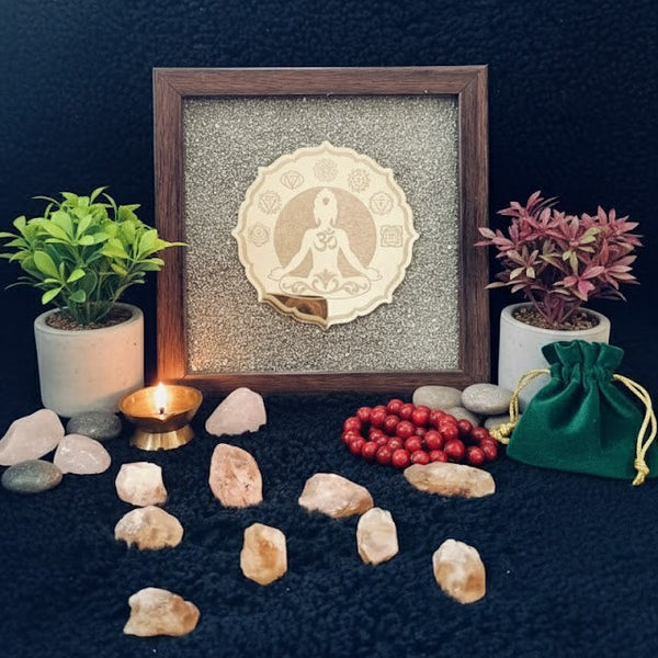 Decorative setup with framed artwork, stones, plants, and a candle on a dark surface.