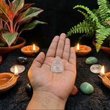 Hand holding a crystal object with candles and plants on a dark surface