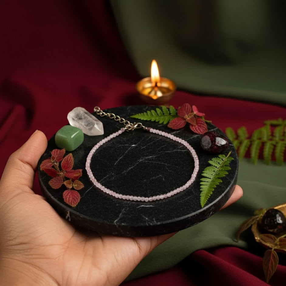 Hand holding a small round black stone with decorative elements and a lit candle in the background.