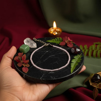 Hand holding a small round black stone with decorative elements and a lit candle in the background.