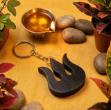 Wooden keychain with flame design on a wooden surface with plants and stones.