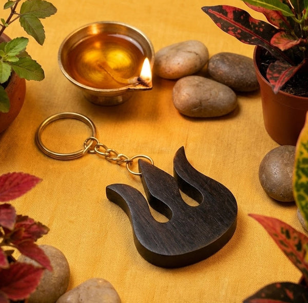 Wooden keychain with flame design on a wooden surface with plants and stones.