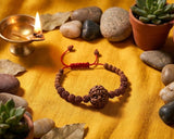 Bracelet with red string on a wooden surface surrounded by potted plants and stones