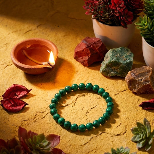 Green beaded bracelet on a textured surface with a lit candle, rocks, and plants.