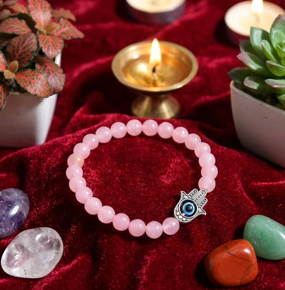 Pink beaded bracelet with a blue eye charm on a red fabric background with candles and plants.