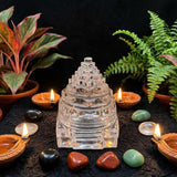 Crystal pyramid with candles and stones on a dark surface with plants in the background