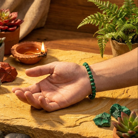 Hand with a green bracelet on a stone surface with plants and a lit candle