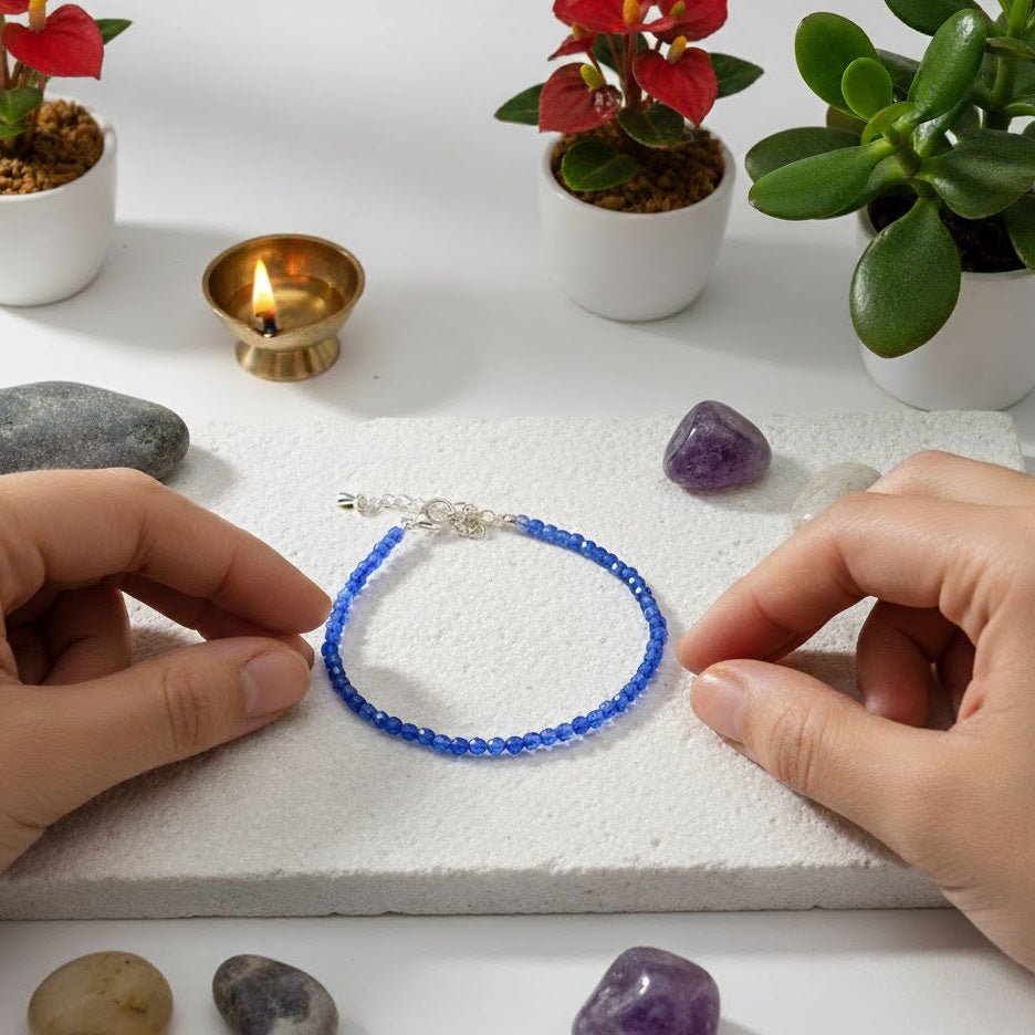 Person holding a blue beaded bracelet with stones and plants on a white surface