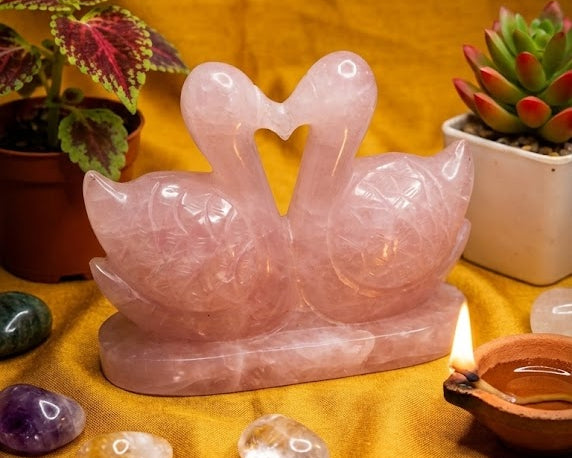 Rose quartz swan sculpture on a yellow fabric background with crystals and candles.