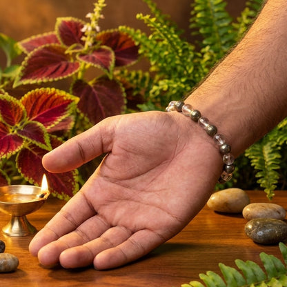 Hand with a bracelet on a wooden surface with plants and a lit candle in the background